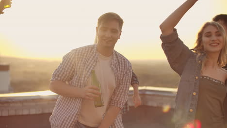 The-boy-moves-his-hands-in-a-dance-and-dances-with-a-beer-with-his-friends-on-the-roof.